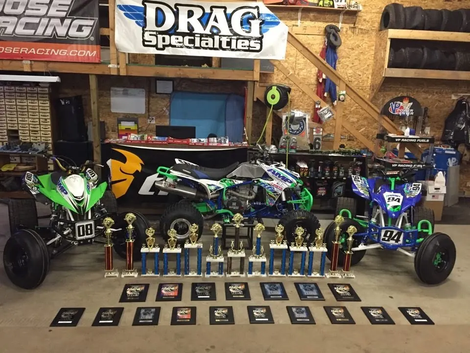 Race quads in AMP colors behind a table of trophies