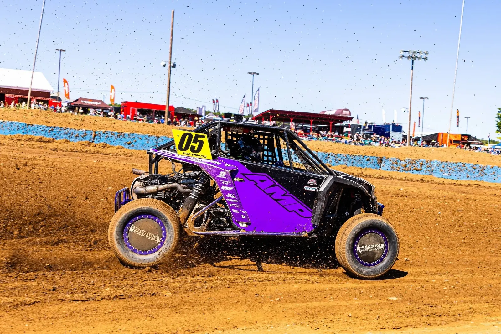 Purple #05 race side-by-side kicking up dirt in a turn