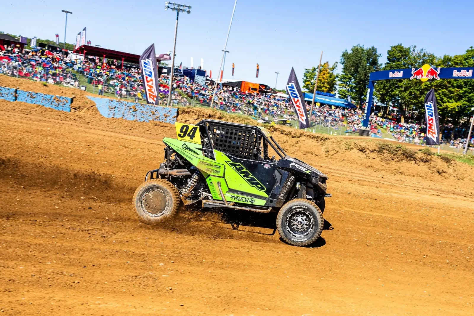 Lime #94 race side-by-side sliding through a dirt-track turn in front of the grandstands
